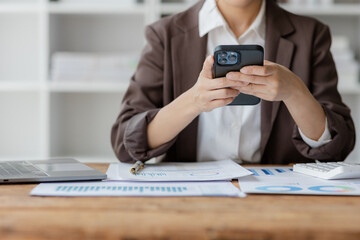 Close-up shot of asian businesswoman using laptop and smart phone for doing financial mathematics on wooden table, tax, accounting, statistics and analytical research concept.