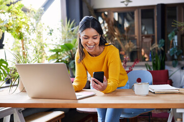 Smiling businesswoman using mobile phone leaning on desk at loft office