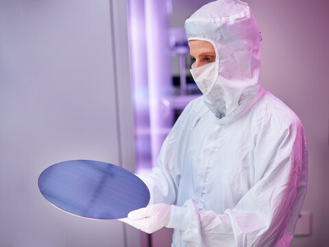 Engineer wearing protective suit holding wafer chip in laboratory
