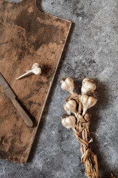 Raw garlic, cutting board and kitchen knife lying on gray surface
