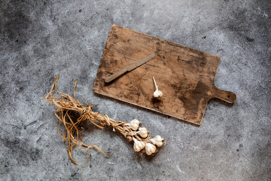 Raw garlic, cutting board and kitchen knife lying on gray surface