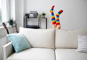 Legs of mature woman wearing rainbow stockings behind sofa at home