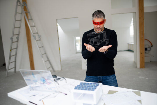 Mature architect wearing virtual reality simulator looking at house model
