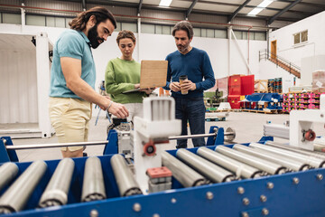 Engineers analyzing machine parts with conveyor belt in foreground