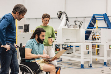 Engineer sitting in wheelchair discussing with colleagues on laptop in factory