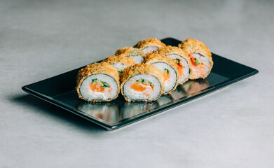 Warm sushi rolls in dried breadcrumbs with salmon on black plate on gray background