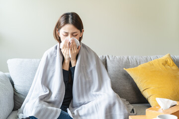 Sick at home concept. Woman sneezing on the sofa in winter season.