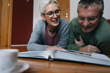 Senior couple lying on the floor at home looking at photo album