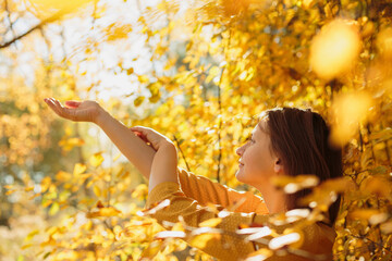 Smiling woman stretching arms amidst golden autumn foliage