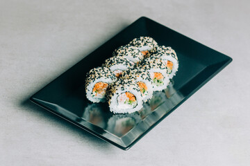sushi rolls in sesame with salmon on black plate on gray background