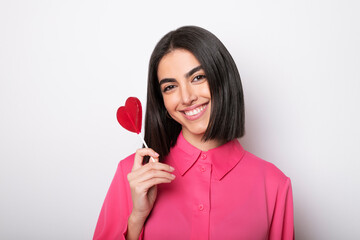 Smiling woman holding heart shaped lollipop against white background