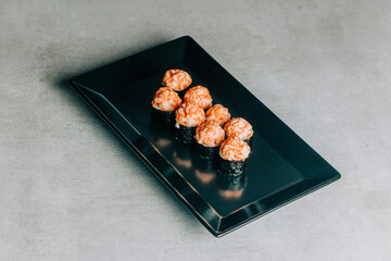 sushi rolls with salmon and caviar on black plate on gray background
