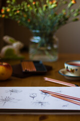 szkicownik na stole, filiżanka jabłko i kwiaty w parcowni