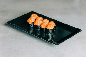sushi rolls with salmon and caviar on black plate on gray background