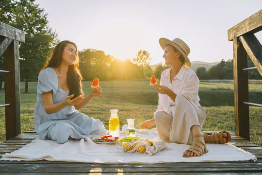Happy women holding slices of watermelon sitting on picnic blanket