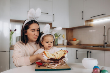 excited mother and child looking at easter bread near easter eggs, decorative rabbits and tulips