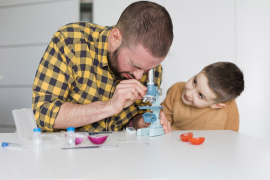 Cute boy watching father looking through microscope at table