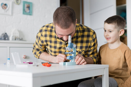 Smiling boy sitting by father looking through microscope at table
