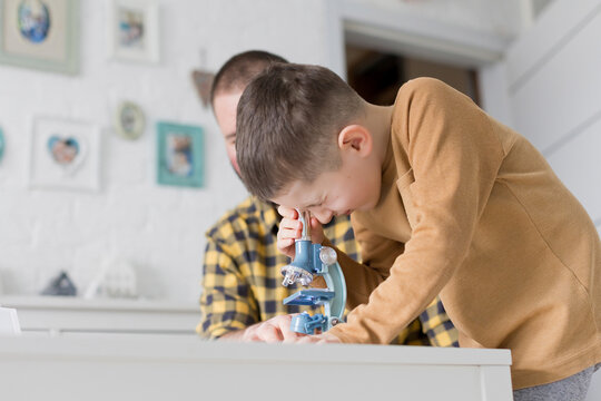 Curious boy looking through microscope at table by father