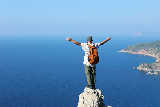 Hiker with arms outstretched standing on edge of cliff looking at sea