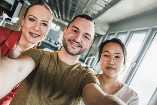 Smiling businessman taking selfie with colleagues at office