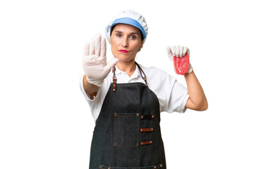 Butcher woman wearing an apron and serving fresh cut meat over isolated background making stop gesture