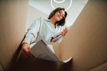 Smiling young woman recycling papers in box at home