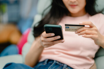 Young beautiful asian woman relaxing on sofa at home using mobile phone and credit card for online shopping Activities on vacation