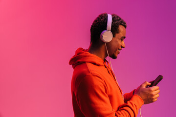 Profile of smiling guy listening music with headphones isolated over pink neon background