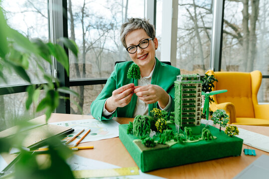Smiling mature wearing eyeglasses businesswoman holding tree model in office