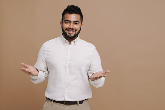 Positive indian man shrugging shoulders isolated over beige background