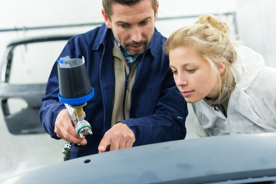 mechanic with paint sprayer training female apprentice