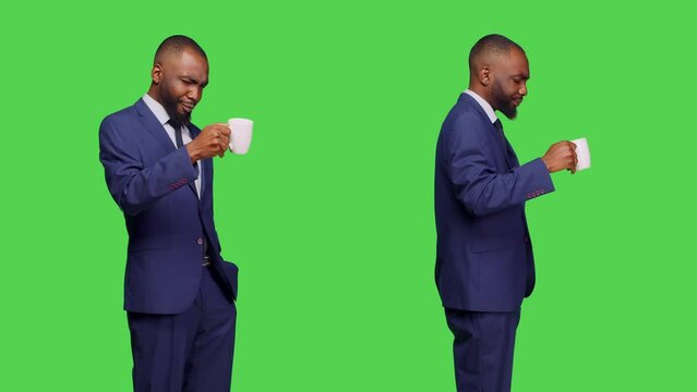 Young corporate manager drinking coffee cup in studio, standing with confidence over greenscreen backdrop. Businessman enjoying caffeine drink or refreshment, optimistic employee.