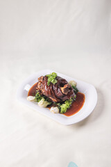 stewed pork trotters whole leg in brown red wine sauce with green vegetables on red cloth background asian chinese western banquet meat menu for restaurant fine dining hotel