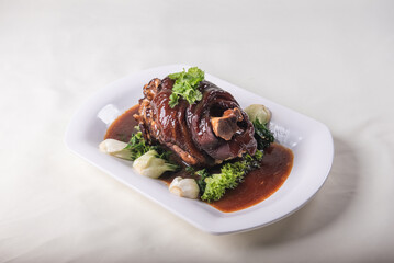 stewed pork trotters whole leg in brown red wine sauce with green vegetables on red cloth background asian chinese western banquet meat menu for restaurant fine dining hotel