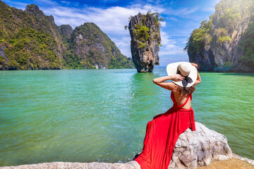 A tourist woman in a red dress looks at the famous sightseeing spot James Bond island at Phang Nga...