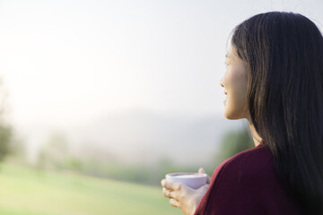 Happy beautiful Asian young woman sitting on the grass field and enjoy relaxing with a stunning...