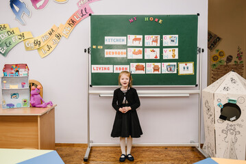 Pupil studies at school and stands near blackboard and answers. Cute schoolgirl reading sounds and letters in classroom at elementary school. Student doing test in primary school. English lesson.