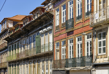 Fototapeta na wymiar Typical Portuguese houses, covered with colorful azulejos, in the historic part of the city of Porto, Portugal. Details of house facades, windows, balconies, railings, colored ceramics.