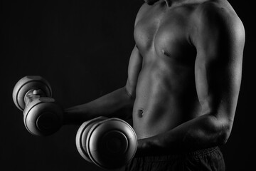 Fototapeta na wymiar Confident young man shirtless portrait training with dumb-bells against black background.