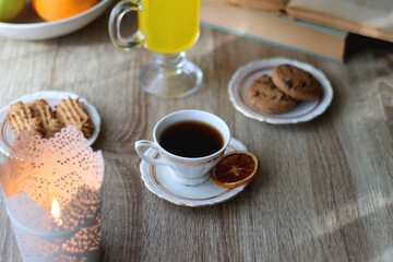 Cup of tea, plates with cookies, glass of orange juice, books, reading glasses, bowl of fruit and candles on the table. Selective focus.