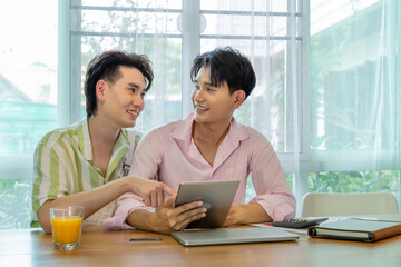 Cute Asian LGBT gay man couple, using tablet online shopping, holding credit card, spend time together. Healthy lifestyle with orange juice.