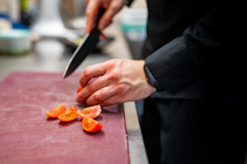 Chef hand cut tomatoes on a chopping board in kitchen