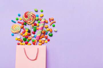 shopping paper gift bag in corner full of assorted traditional candies falling out on colored background with copy space. Happy Holidays sale concept