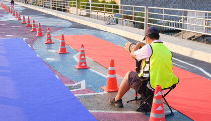 Rear side view of Asian photographer taking picture of charity marathon participants while running on coastal bridge