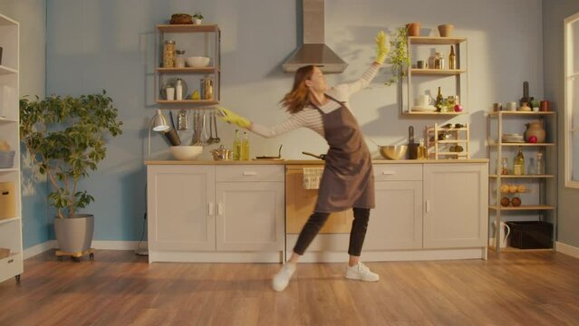 Creative Woman Dancing at Home in Kitchen Enjoying Housework. Happy Young Woman Cute Housewife is Listening to Music and Dancing During Domestic Work. Household Chores Concept.