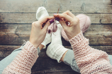 woman hands knitting small baby socks, top view. 