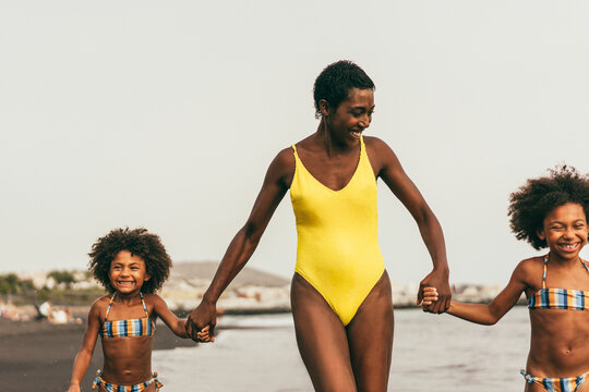 African sisters twins running on the beach with smiling mother - Focus on left hands - Mum day concept