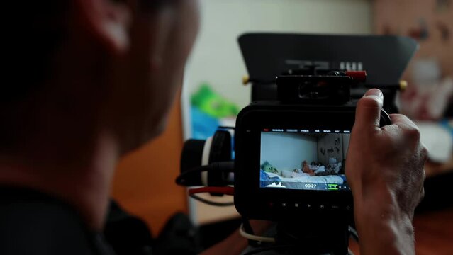 Cameraman operator with digital cinema camera shoots bed in kid's room, backstage filming movie indoors. Cinematography. Production of commercial ad TV series. Black device, magic design. Videography