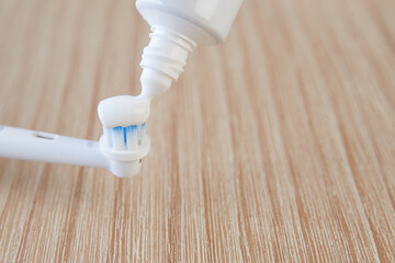 Dental health concept. Toothpaste tube squeezing toothpaste over toothbrush over wooden background
